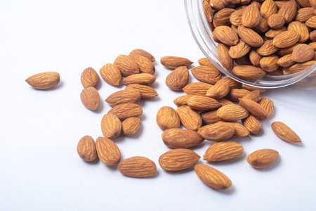 Almonds falling from a glass container leaning against a white background, close upの写真素材
