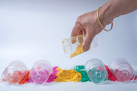 Indian woman hands pouring yellow colored holi powder into glass jars. Indian festival Holi backgroundの写真素材