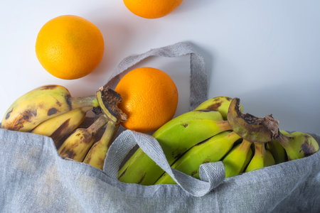 Fresh bananas and oranges in a linen bag on a white background. Top viewの写真素材
