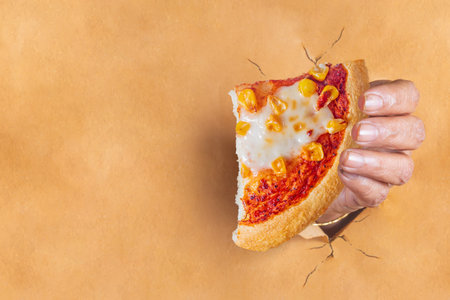 Indian woman's hand holding a slice of pizza that comes out after tearing the brown paper with space...