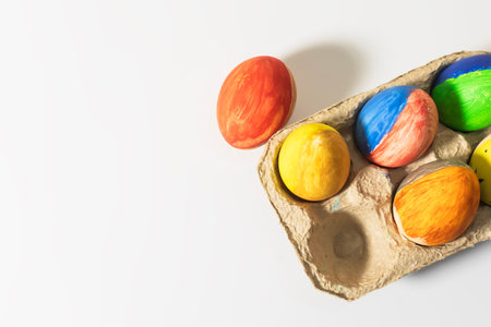 Colorful Easter eggs in a cardboard box on a white background. Top view