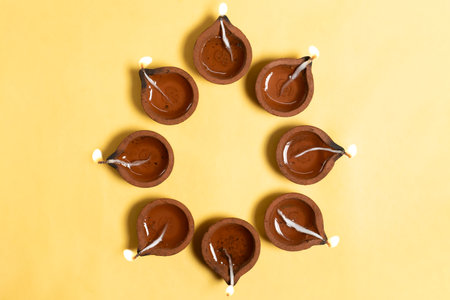 Happy Diwali - Traditional clay diya lamps are lit in a floral pattern on a yellow background during Diwali festival celebrations.の写真素材