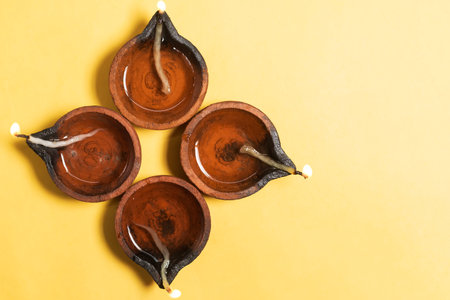 Happy Diwali - Traditional clay diya lamps are lit in a floral pattern on a yellow background during Diwali festival celebrations. Copy space for text.の写真素材