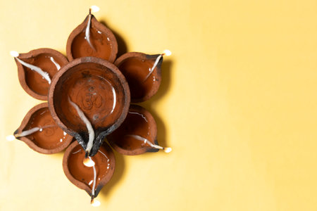 Happy Diwali - Traditional clay diya lamps are lit in a floral pattern on a yellow background during Diwali festival celebrations. Copy space for text.の写真素材