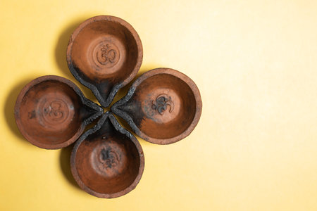Close-up view of four traditional mud diyas arranged in floral pattern on yellow background with...