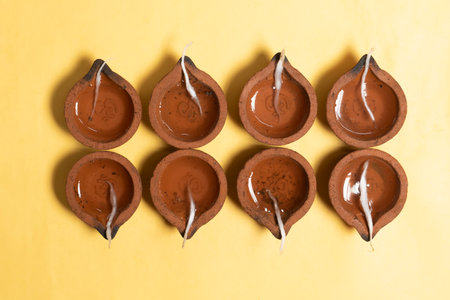 Traditional clay oil lamps are arranged in a symmetrical pattern on a vibrant yellow background for Diwali celebrations.の写真素材