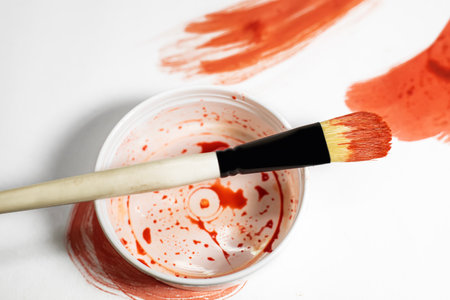 Paint brush on top of paint can with red paint on white background.の写真素材