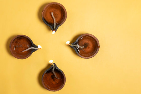 Happy Diwali - Overhead view of glowing clay diyas on vibrant yellow background with space for textの写真素材