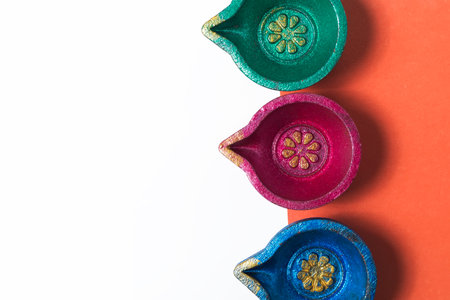 Three vibrant, traditional Diwali oil lamps set against an orange and white background, perfect for festive designs, holiday greetings, and cultural celebrations.の写真素材