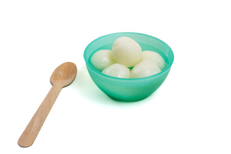 Traditional Indian sweet rasgulla in green plastic bowl with wooden spoon on white backgroundの写真素材