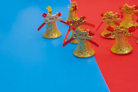 A festive holiday composition featuring golden Christmas bells adorned with vibrant red bows, set against a striking split blue and red background.の写真素材