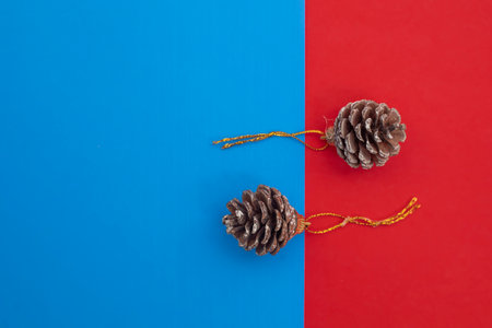 Elegant brown pine cones adorned with golden loops, set against a vibrant blue and red dual background. ideal for seasonal themes and decorative designs.の写真素材