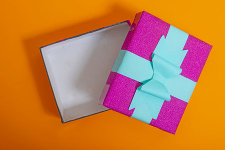 Empty gift box with colorful wrapping and bow against a bold orange backdrop, representing celebration, surprises, and festivity. ideal for parties, holidays, or special occasions.の写真素材