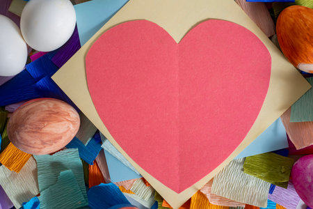 A top view of a red heart surrounded by colorful craft paper and decorated eggs, perfect for Easter...