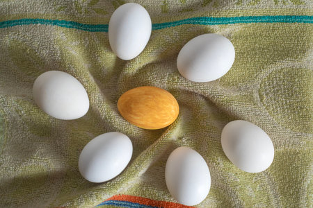 A golden egg surrounded by white eggs on a soft green cloth. Top view