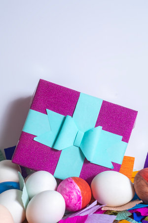 A vibrant gift box adorned with blue ribbon, surrounded by eggs and colorful decorations. perfect...