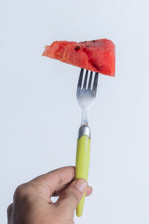 A vibrant and juicy triangular slice of watermelon held on a fork with a yellow handle. ideal for healthy eating and tropical themes.の写真素材