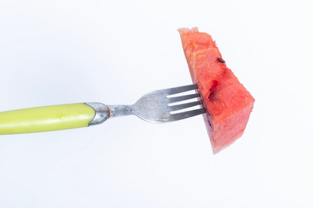 A wedge of vibrant juicy watermelon pierced with a fork, isolated on a clean white background.の写真素材