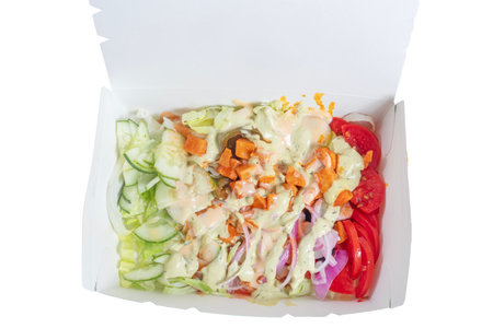 A freshly prepared salad served in a takeout box, including cucumbers, tomatoes, and lettuce with a creamy dressing, offers a healthy and nutritious meal option.の写真素材