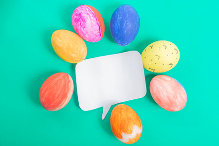 Easter eggs arranged in a circle around a blank speech bubble, set on a bright green background, perfect for seasonal and festive design purposes.の写真素材