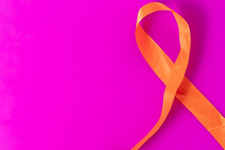 The orange awareness ribbon is positioned diagonally on a bright pink background to represent awareness, support, and compassion.の写真素材