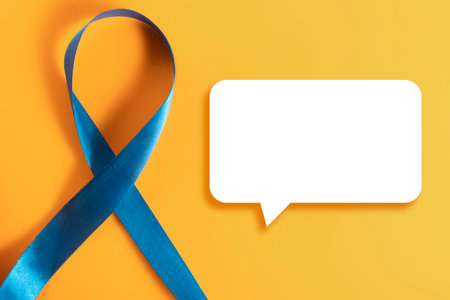 A blue symbolic awareness ribbon placed on a vibrant yellow background with a white speech bubble.の写真素材
