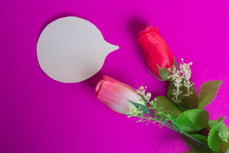 Artificial red and pink roses sit on a pink background with a blank speech bubble. Perfect for romantic themes, message concepts, and Valentine-related designs.の写真素材