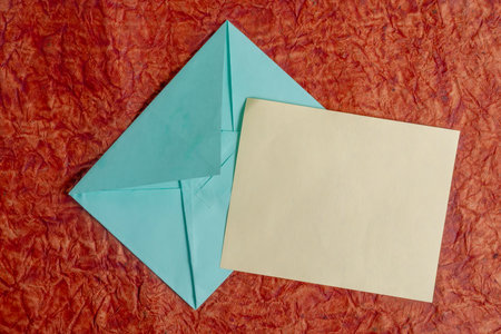 An overhead view of a blank piece of paper and a blue envelope placed on a red background. Perfect...