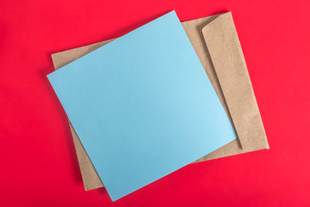 The blue paper and brown envelope are beautifully arranged on a vibrant red surface, showcasing a minimalist design.の写真素材
