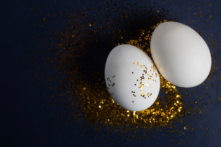 White eggs decorated with gold glitter are set on a dark surface, evoking the elegance of Easter.の写真素材