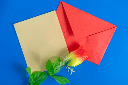 Top view of a red envelope with a blank card and artificial flower on a blue background for Valentine's Day.の写真素材