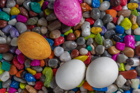 Colored Easter eggs, including white, pink, and yellow, lie a top a bed of multicolored pebbles. perfect background for spring celebrations, and festive occasions.の写真素材