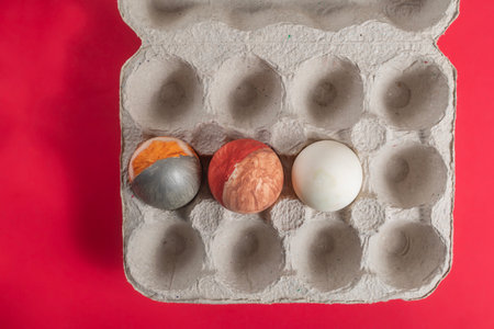 An overhead view of three colorful eggs placed in an open cardboard box set on a bright red surface provides a festive and creative display perfect for holiday decorations, Easter, and artistic expression.の写真素材