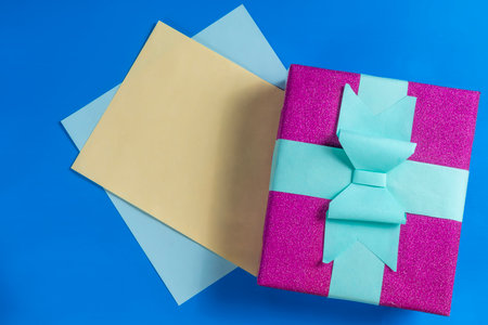 A bright purple gift box decorated with a teal bow embedded in colorful sheets on a blue surface. For celebration, gift giving and festive occasions, a surprise.の写真素材