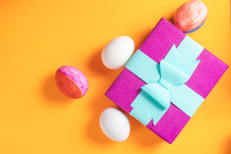 The Easter gift box, and the decorative eggs arranged on an orange surface, symbolize festive spring celebration and joyful holiday moments.の写真素材