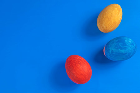 Three colorful Easter eggs in red, yellow, and blue are set against a bright blue background, a minimalist design great for celebration or seasonal projects.の写真素材