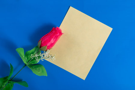 A single red rose and blank yellow paper on a vibrant blue surface representing love, messages and creative ideas. Perfect for love concepts.の写真素材