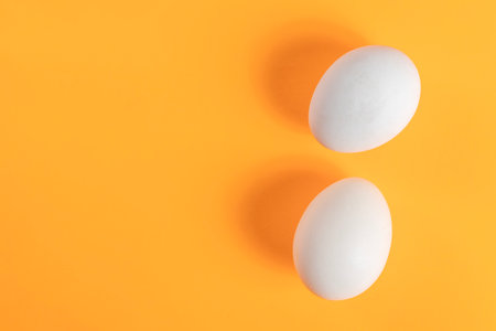 Two white eggs placed on an orange background create a colorful and minimalist composition, perfect for art or kitchen related themes.の写真素材