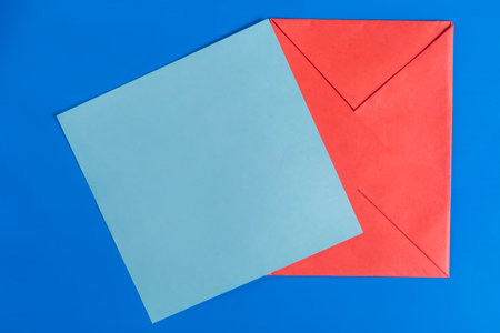 Top view of a red envelope with a blank blue paper card on a bright blue background.の写真素材