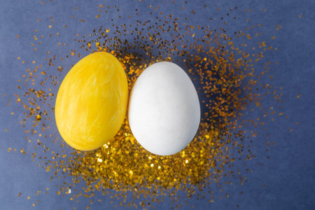 Decorative yellow and white eggs on a blue background, surrounded by shimmering gold glitter, symbolize creativity and celebration.の写真素材