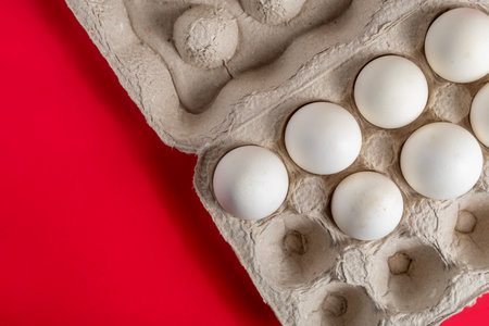 A display of white eggs placed inside a carton, with a bright red background, is perfect for food freshness concepts.の写真素材