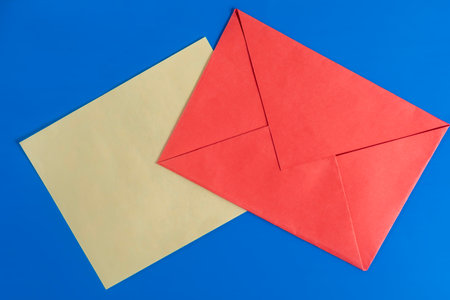 A vibrant image of a red envelope with brown paper attached on a blue background. Suitable for communication, correspondence, and messaging.の写真素材