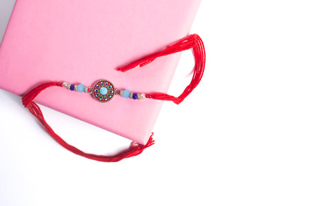 An elegant rakhi with vibrant beads and red thread, creatively displayed in a pink gift box, is...