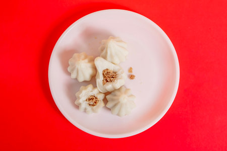 Steamed sweet modak rice dumplings arranged on white plate against a bright red background. displays...