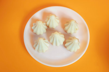 Steamed sweet modak rice dumplings arranged on white plate on yellow background. Perfect for Ganesh...
