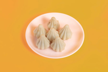 Steamed sweet modak rice dumplings arranged on white plate on yellow background. Perfect for Ganesh...