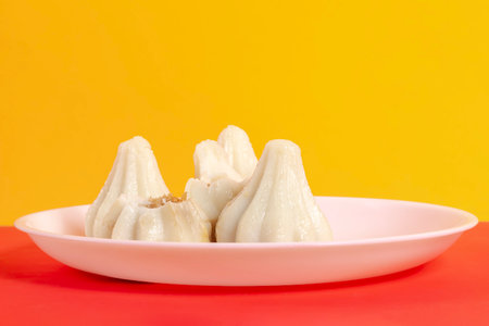 Steamed sweet modak rice dumplings are arranged on a white plate, against a vibrant yellow...