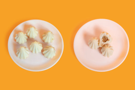 Steamed sweet modak rice dumplings arranged on white plates over a yellow background. One plate has...