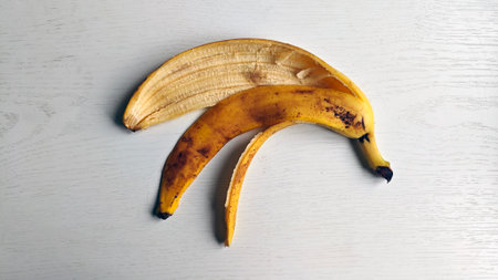 Peeled banana skin lying on white wooden surface. Banana peel has some brown spots, indicating ripe. Banana peel is curved and has yellow color with some brown spots. Organic waste.の写真素材