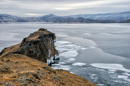 Baikal Lake and rock in the December cold. Time of freeze-up. Ice floes is swiming on the waterの写真素材